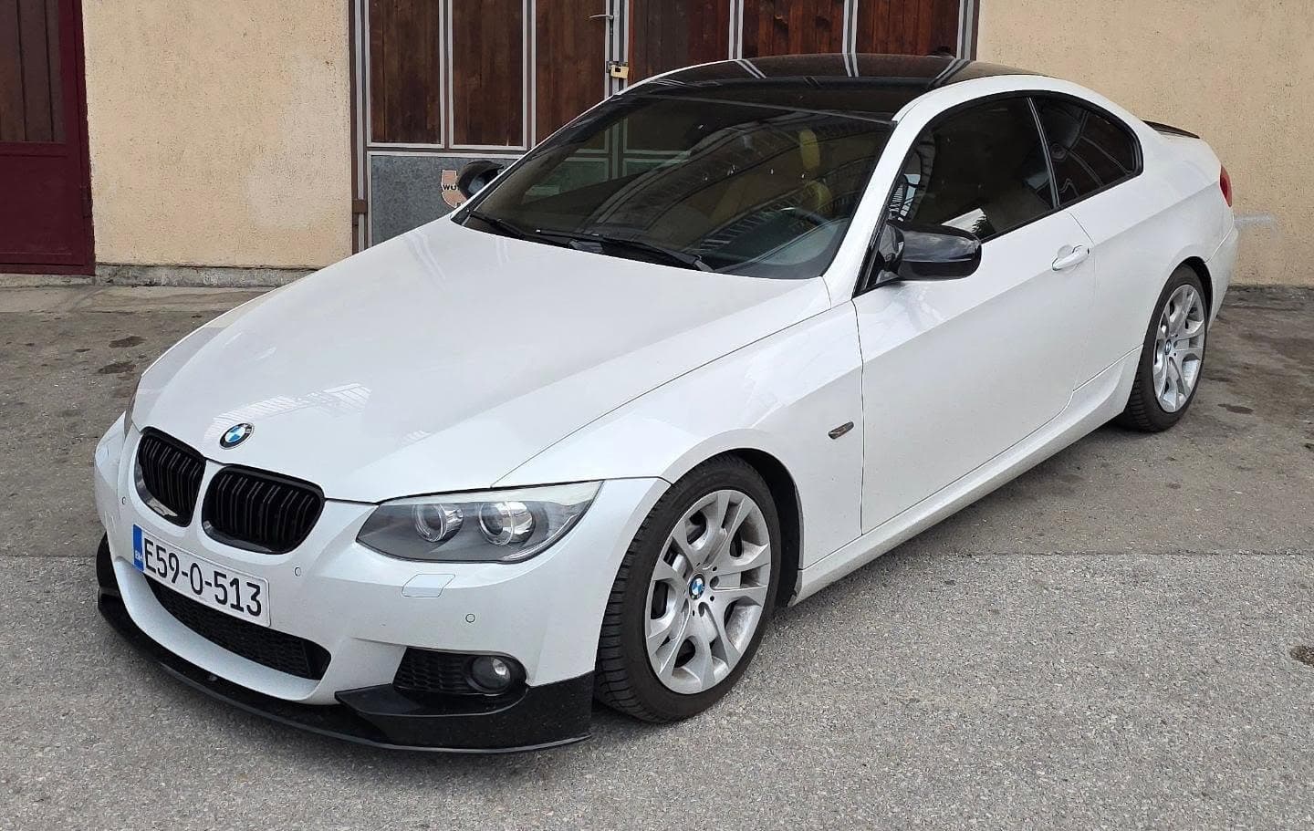 Bijeli BMW 320d Coupé E92 LCI iz poluprofila, ispred garaže